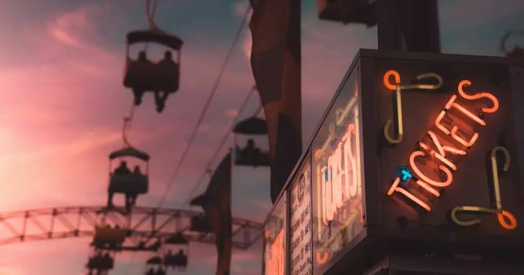 Silhouettes of cable cars against a vibrant sunset sky, with a neon "Tickets" sign in the foreground.