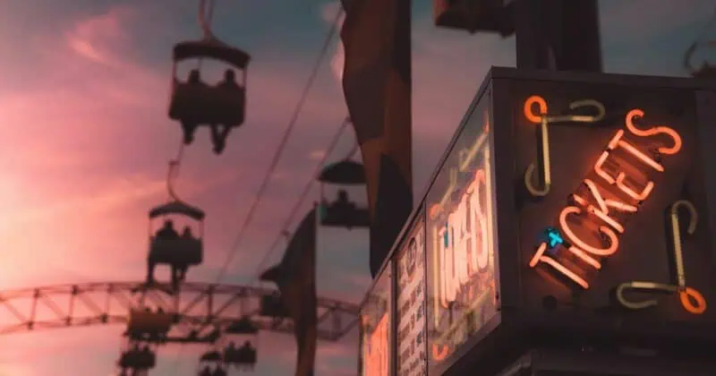 Silhouettes of cable cars against a vibrant sunset sky, with a neon "Tickets" sign in the foreground.