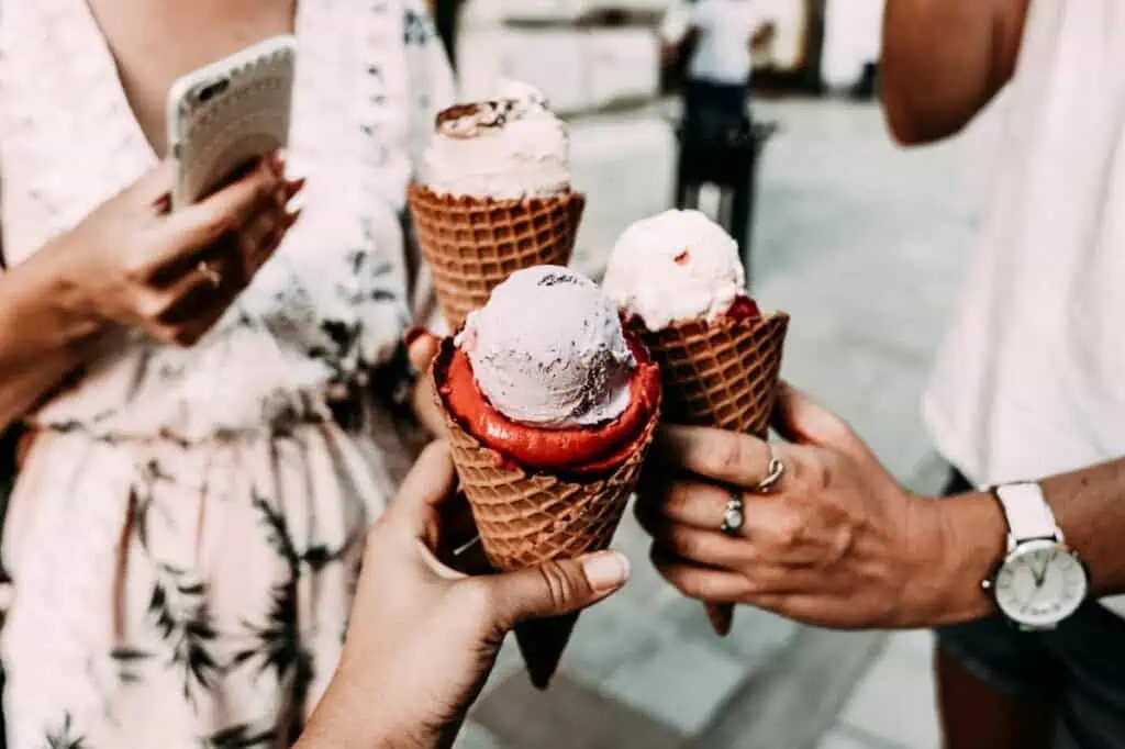 Close-up of hands holding waffle cones with colorful ice cream scoops