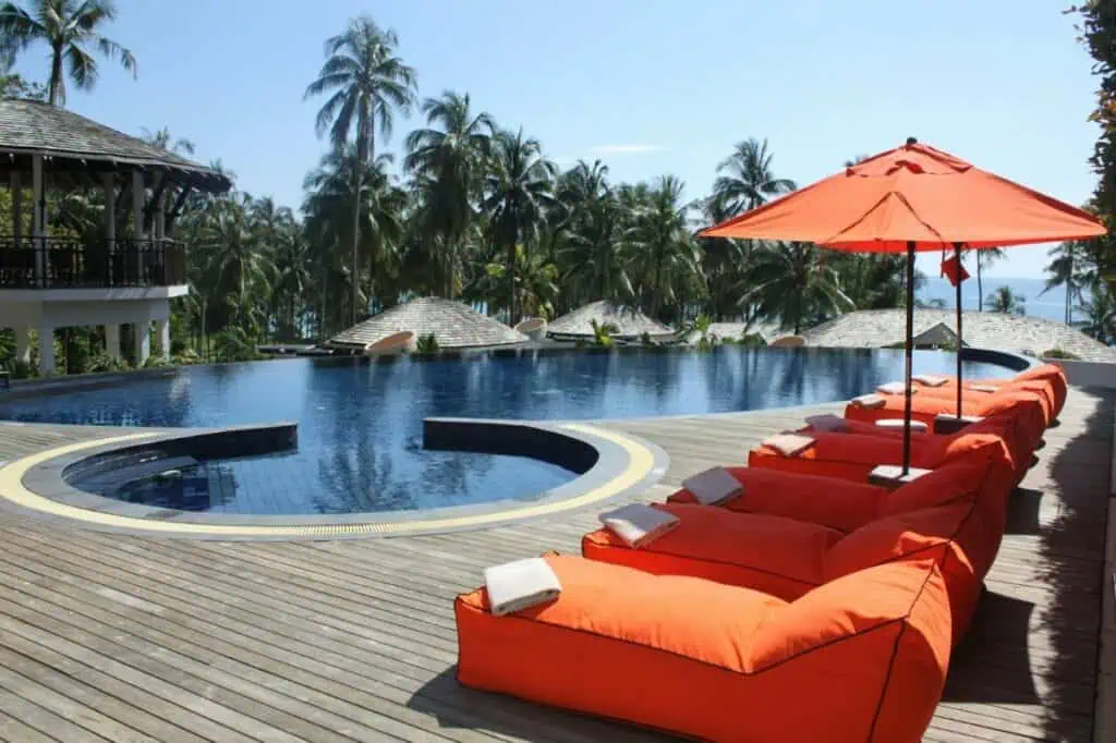 Infinity pool with orange lounge chairs overlooking palm trees and ocean