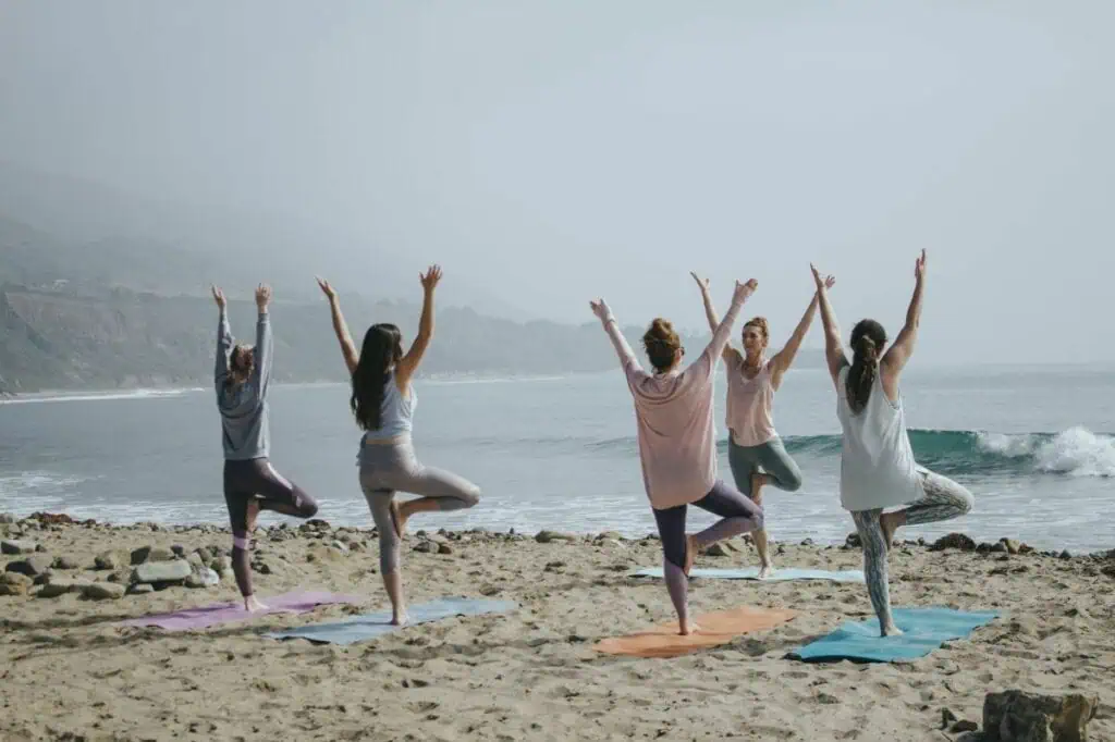 Five women doing tree pose yoga on a foggy beach