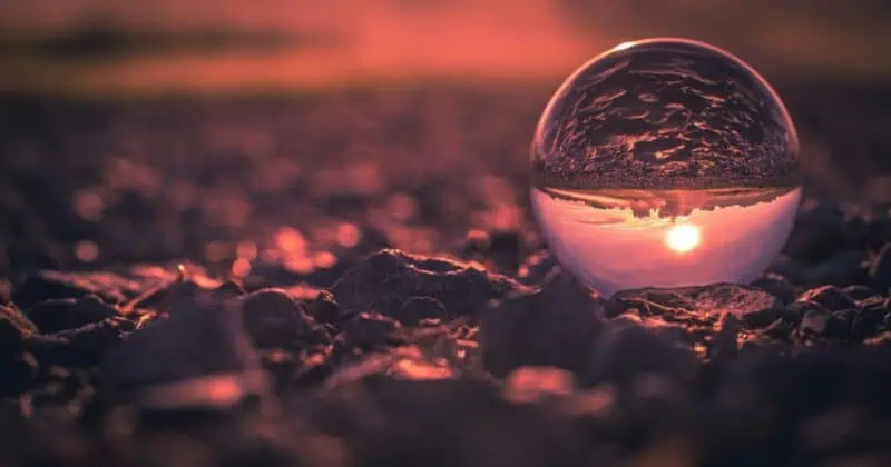 Crystal ball on rocky surface reflecting sunset sky in pink and orange hues