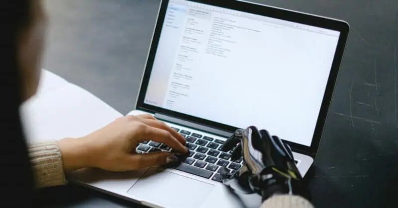 Person typing on laptop with hands visible on keyboard, screen showing text document